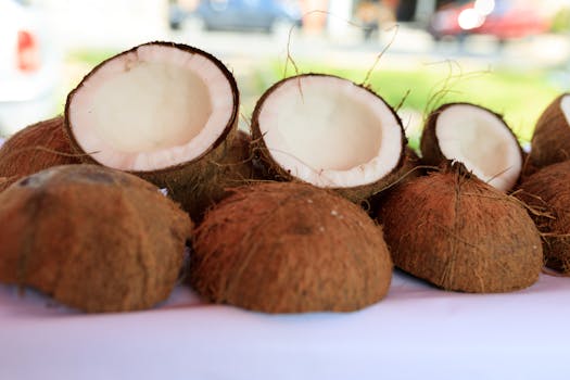 Halved coconuts on a white surface outdoors, showcasing their fibrous texture and white flesh.