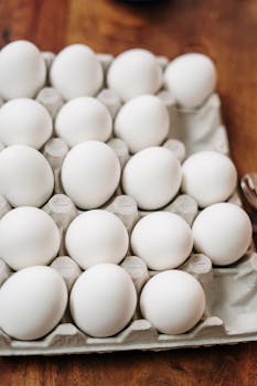 A carton of fresh organic white eggs displayed on a wooden table, perfect for culinary uses.